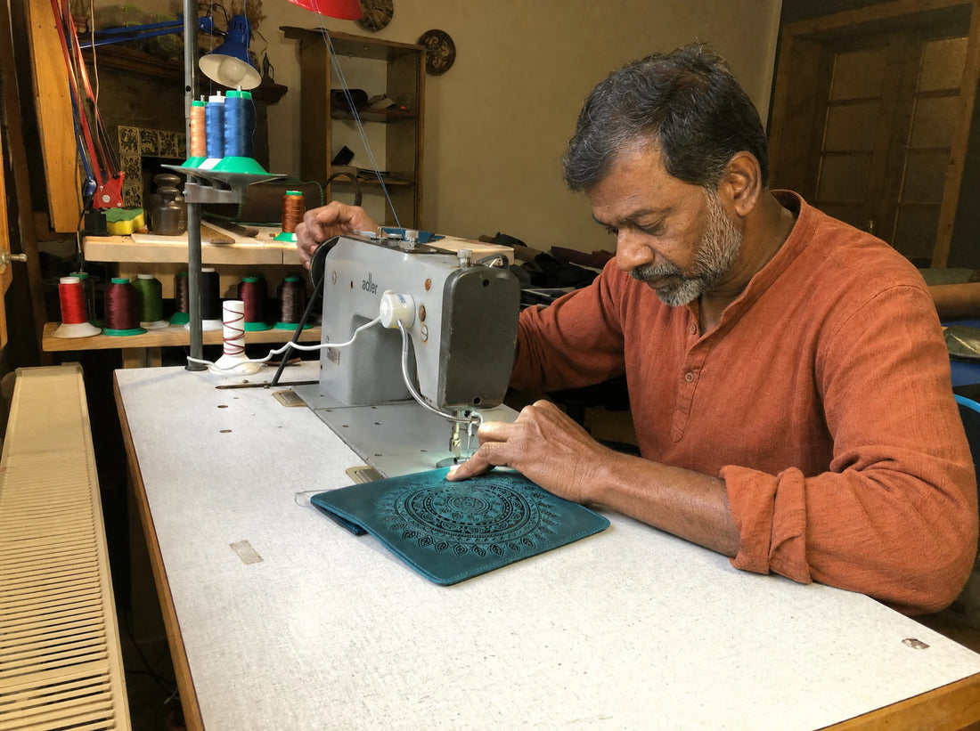 Artisan stitching a dark-teal hand-tooled mandala wallet at the workshop sewing machine